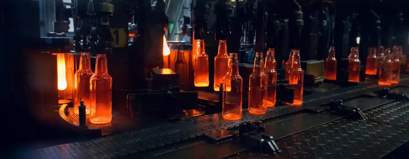 Conveyor belt moving hot glowing glass bottles inside a factory