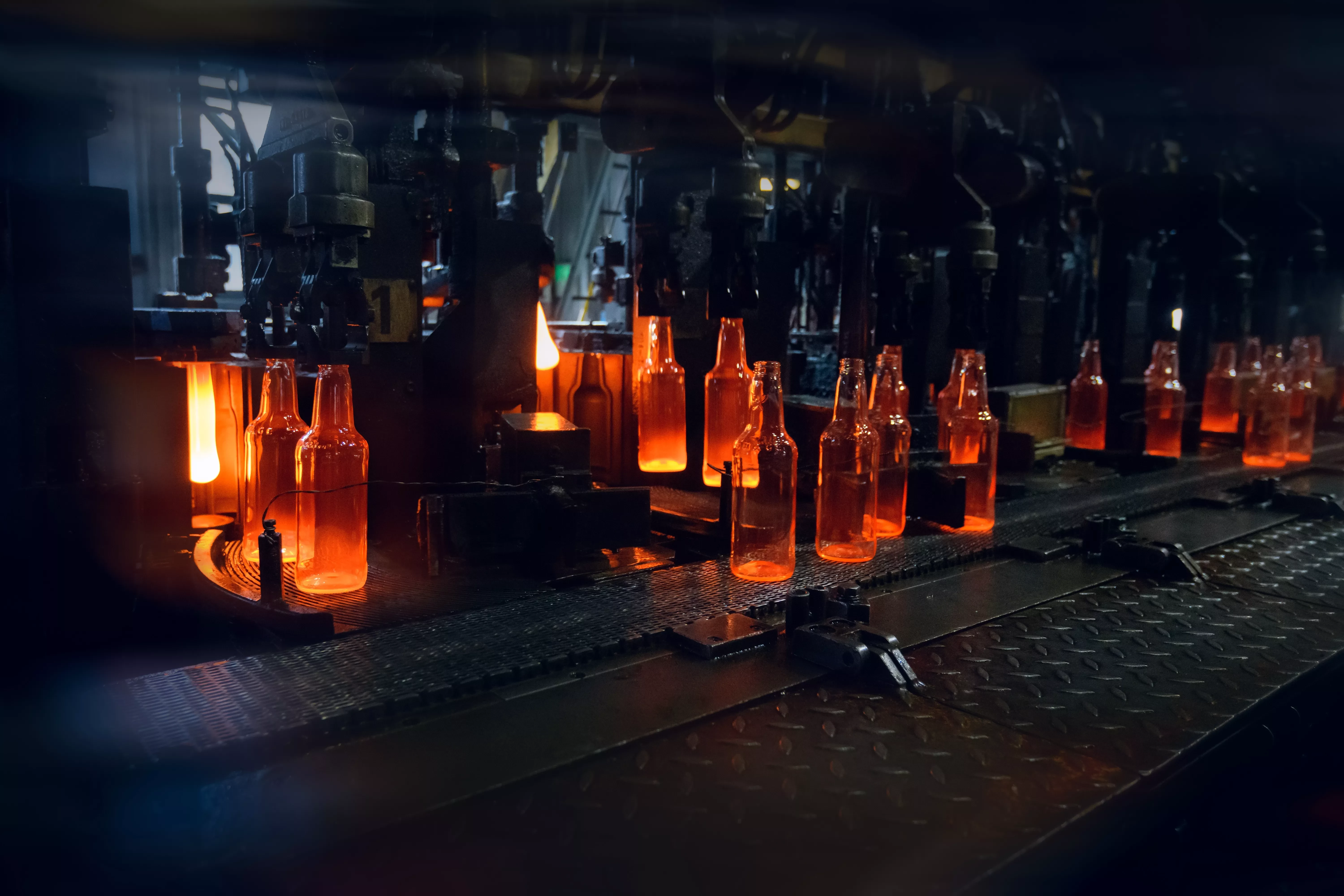 Conveyor belt moving hot glowing glass bottles inside a factory